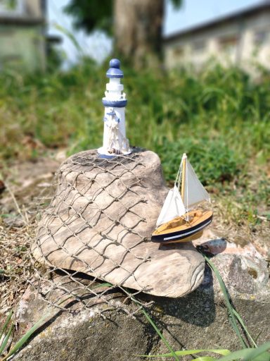 Wurzelholz mit Leuchtturm, Segelboot und einem Fischnetz Kleine maritime Landschaft aus einem Wurzelholz mit einem Leuchtturm und einem kleinen Segelboot und einem Fischnetz